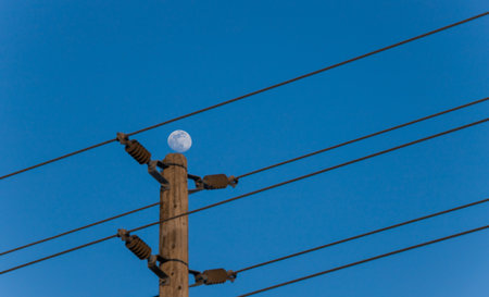 Full moon on electric pole with wires against blue sky in the eveningの写真素材