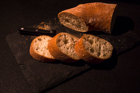 Fresh crispy sliced bread on black board and knife, on a black background with copy space. Old...