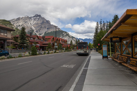 Public transportation - electric city bus in Banff. Alberta Tourism in mountains. Downtown road with houses, bus stop and mountain on backgroundのeditorial素材