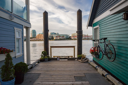 Houseboats with colorful exteriors, one blue and one green, line a wooden pier. A bicycle is mounted on the side of the green house, and potted plants.  Victoria, BC, Canadaの写真素材