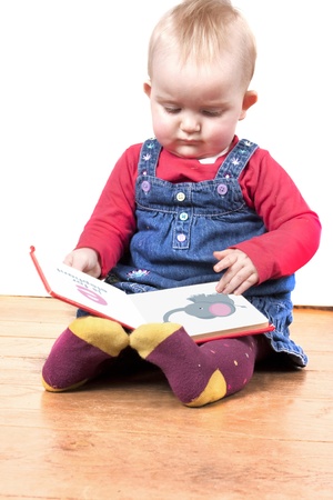 baby girl reading a small picture book isolated on white backgroundの写真素材