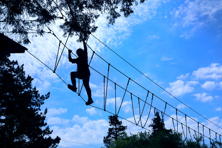 silhouette of boy climbing and taking on the challenge of a high ropes obstacle challenge courseの写真素材