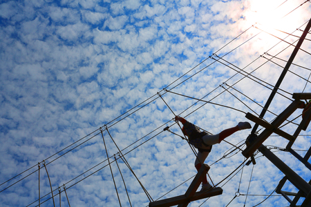 boy climbing and taking on the challenge of a high ropes obstacle challenge courseの写真素材
