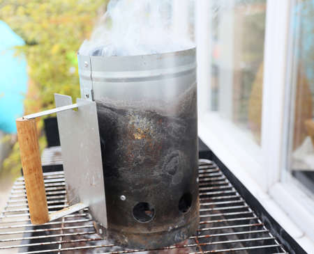 starting a bbq with a smoking chimney with briquettes and smoke insideの写真素材