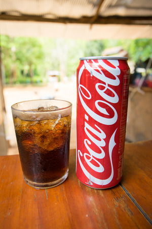 PAI THAILAND 23 MAY 2017: Coca-Cola can drink and a glass of coke with ice cubes over wooden table in Pai Thailandのeditorial素材