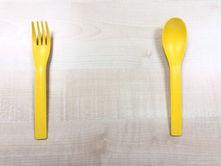 Yellow small plastic spoon and fork on the wood table