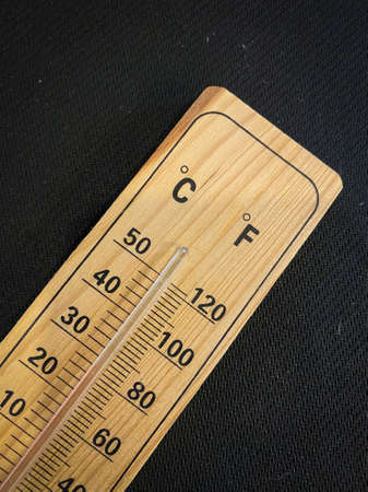 Analogue wooden thermometer with red measuring liquid on black background