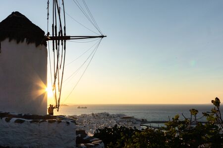 Young male in shorts standing on the edge next to windmill witnessing sunset at Mykonos , Greeceの写真素材