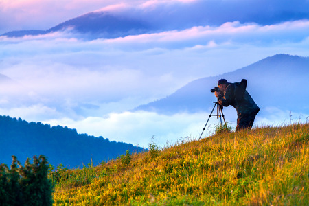 The photographer does a picture at sunset in the misty mountainsの写真素材