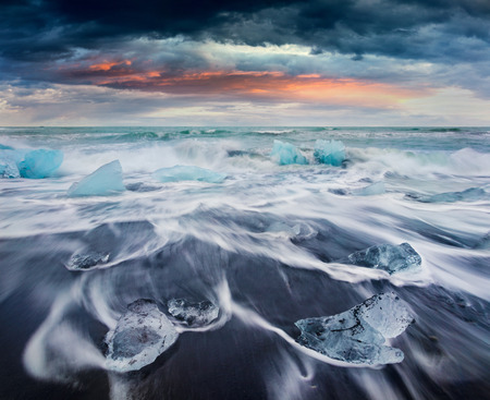 Blocks of ice washed by the waves on Jokulsarlon beach. Dramatic summer sunrise in Vatnajokull...