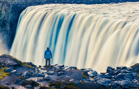 Tourist admiring view of falling water of the most powerful waterfall in Europe - Dettifoss. Jokulsargljufur National Park, Iceland. White nights view. Artistic style post processed photo.の写真素材
