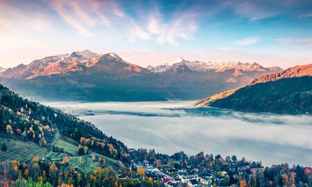 Splendid view of Zell lake in the morning mist. Foggy autumn sunrise of Austrian town - Zell am See, south of the city of Salzburg. Beauty of nature concept background.の写真素材