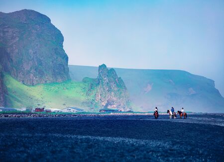 Horseback riding on the famous Black Sand Beach in Vik village. Amazing summer scene of Icelan,...