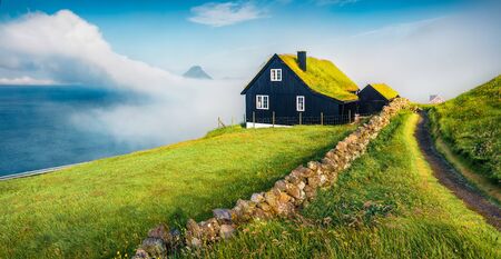 Foggy summer view of Velbastadur village with typical turf-top houses. Amazing morning scene of Streymoy island, Faroe, Kingdom of Denmark, Europe. Traveling concept background.の写真素材
