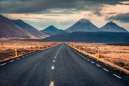 Empty asphalt road with dramatic cloudy sky. Typical icelandic landscape with volcanic hills. Image...