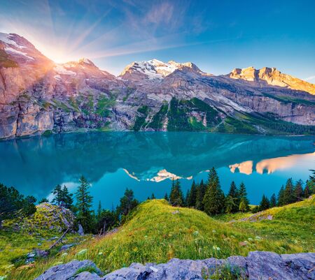 First sunlight gloving mountain hills and meadows. Picturesque summer view of unique Oeschinensee Lake. Sunrise in Swiss Alps with Bluemlisalp mountain on background, Switzerland, Europe.の販売画像