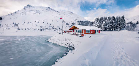 Traditional Norwegian red wooden houses on the shore of frozen fjord. Bright winter scene of Lofoten...