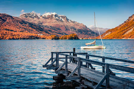 White yacht on the Sils lake. Orange larch trees forest in Swiss Alps. Colorful autumn view of Switzerland, Europe. Traveling concept background.の写真素材