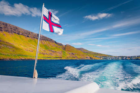 Faroe Islands flag on a motor boat. Picturesque summer seascape of Atlantic Ocean. Amazing morning view of Faroe islands, Denmark, Europe. Travel concept background.の写真素材