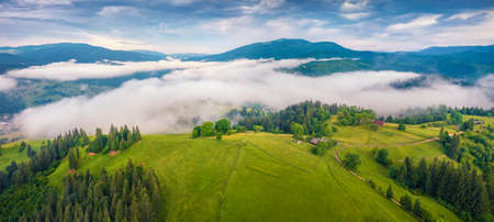 beautiful summer scenery. Morning fog spreads on the mountain valley. Panoramic summer scene of Carpathian village. Amazing morning landscape of mountain hills, Ukraine, Europe.の写真素材