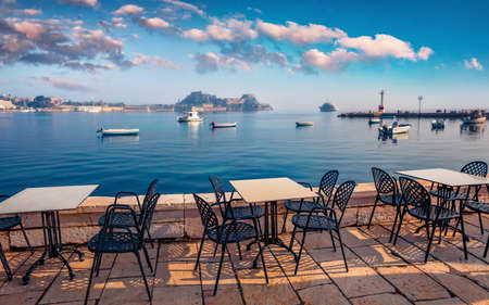 Spectacular summer seascape of Ionian Sea, Corfu island, Greece, Europe. Picturesque morning view of cozy seaside restaurant with old Venetian fortress in Kerkira town on background.の写真素材