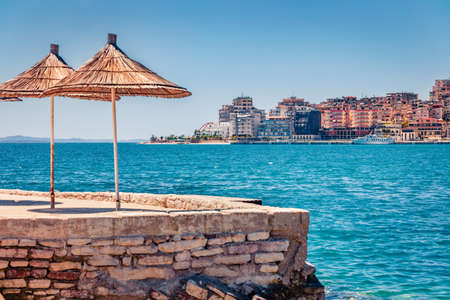 Sunny spring cityscape of Saranda tiwn. Amazing summer view of Albanian Riviera, in southern Albania, Europe. Captivation morning scene of Ionian sea with straw umbrellas.の写真素材