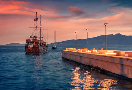 Wooden sailboat on the shore of Saranda port. Amazing spring sunset on Ionian sea. Illuminated evening scene of Albania, Euroepe. Travel concept background.の写真素材