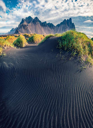 Spectacular summer view of Stokksnes cape with Vestrahorn (Batman Mountain) on background. Incredible Icelandic landscape with black sand dunes with fresh green grass on top.の写真素材