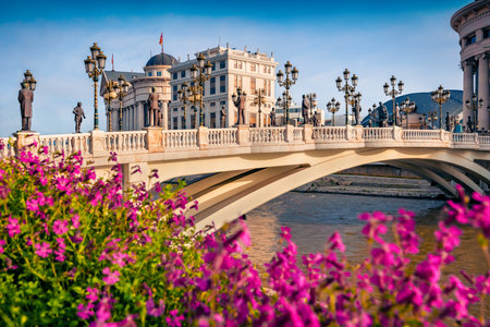 Blooming violet flowers on the shore of Vardar river. Splendid spring cityscape of capital of North Macedonia - Skopje with Archaeological Museum. Colorful view of Art Bridge.のeditorial素材