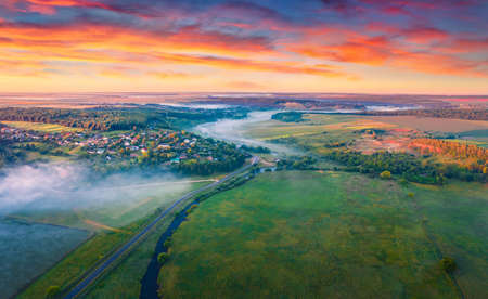Captivating summer sunrise in Ukrainian countryside. Aerial morning view fron flying drone of small foggy lake and asphalt road. Beauty of countryside concept background.の写真素材