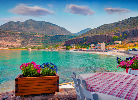 Stunning summer cityscape of Neo Itilo village. Hospitable cafe on the shore of Ionian sea with a pot of blooming flowers. Sunny morning scene of Peloponnese peninsula, Greece, Europe.の写真素材