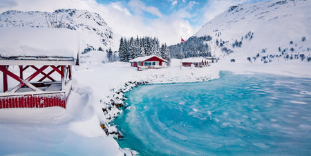 life over polar circle. Traditional Norwegian red wooden houses on the shore of frozen fjord. Panoramic winter view of Kongsjordpollen fjord, Lofoten islands, Vestvagoy, Norway, Europe.の写真素材