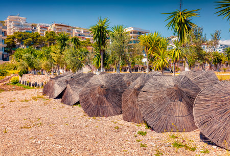 First warm days in Saranda resort. Straw umbrellas on the shore of the Ionian sea. Sunny morning scene of Albania, Europe. Travel concept background.の写真素材