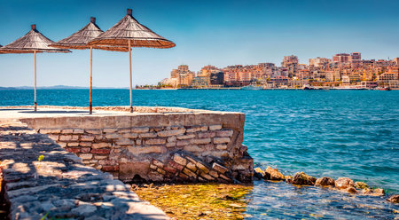 Charming spring cityscape of Saranda tiwn. Marvelous summer view of Albanian Riviera, in southern Albania, Europe. Superb morning scene of Ionian sea with straw umbrellas.の写真素材