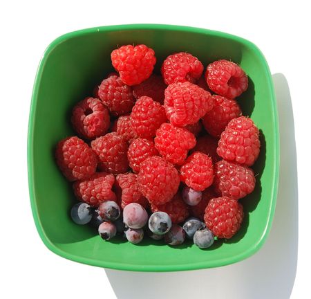 Freshly picked raspberries and blueberries in a green bowl 