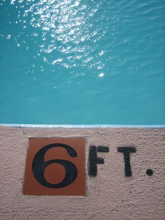 A swimming pool-side depth indicator, with water glinting in the sun 