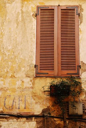 A newly painted window with shutters contrasts with the old cafe sign painted on the wall below it, Italy の写真素材