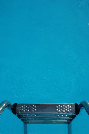 Steps lead down into the clear blue waters of a well kept swimming pool 