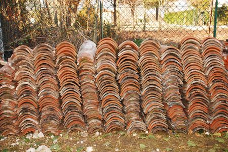A pile of old terracotta tiles in a rural garden. The tiles have been salvaged from a roof of an old farm building during demolitionの写真素材