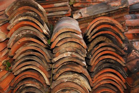 A pile of old terracotta tiles in a rural garden. The tiles have been salvaged from a roof of an old farm building during demolitionの写真素材