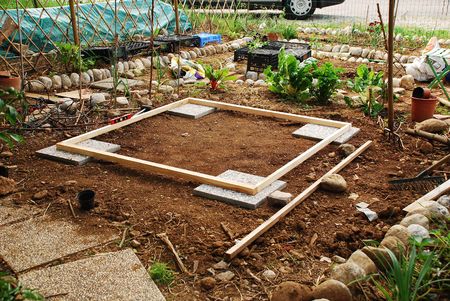 A small patch of land which has been levelled in preparation for the construction of a garden shed. Flagstones mark the corner while the level is checked by a level and beamsの写真素材