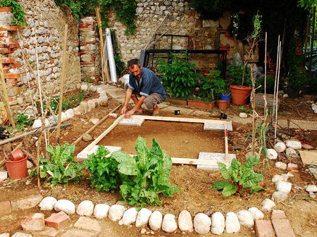A man prepares a small patch of land which has been levelled in preparation for the construction of a garden shed. Flagstones mark the corner while the level is checked by a level and beamsの写真素材