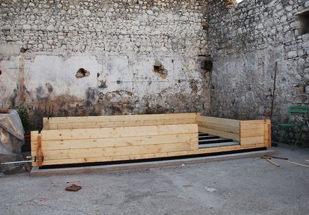 A concrete base for building a small prefabricated wooden cabin on. The cabin's wooden foundation beams have been placed ontop of the concrete base and the first few wall beams have been placed. It is  located within the old stone walls of a now derelict の写真素材