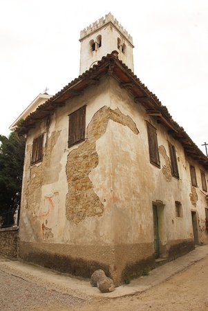 An old corner house in the historic village of Smartno in Goriska Brda, Slovenia. A church bell tower can be seen towering over the roof of the abandoned houseの写真素材