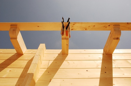 Exterior roof detail on a partially constructed wood (fir) block house, a pre-cut wooden house which is assembled on-site. This shot shows the first layer of roof cross beams being clamped in place の写真素材