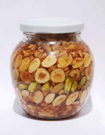A jar of Greek honey and nuts  pistachios, peanuts, hazelnuts, pine nuts, almonds, walnuts  in natural lightの写真素材