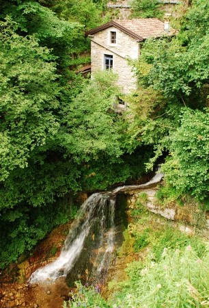 An abandoned stone building near a small waterfall in a stream in rural north east Italy の写真素材