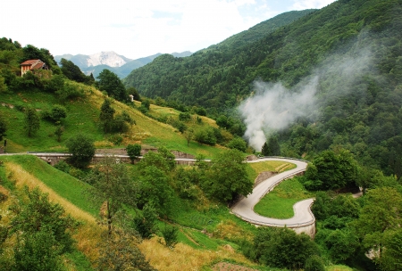 A view of a winding country road in the Carnic Alps near Paularo in the north eastern Italian region of Friuli  A small fire can be seen near the side of the road where a farmer is burning grasses の写真素材
