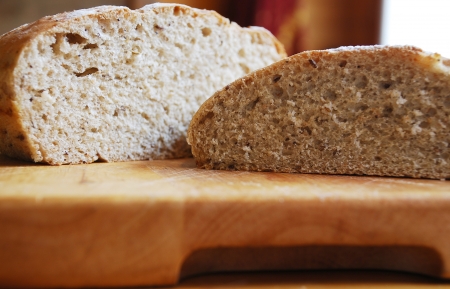 Two loaves of home-baked sourdough bread on a wooden chopping board on a wooden table in natural lightingの写真素材