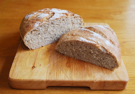 Two loaves of home-baked sourdough bread on a wooden chopping board on a wooden table in natural lightingの写真素材